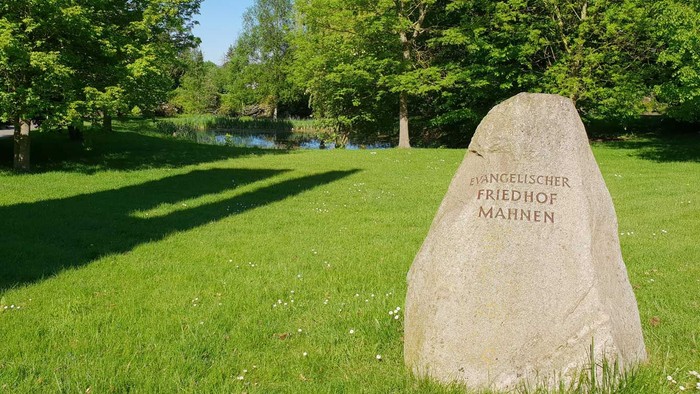 Eine Wiese mit Teich, darauf ein Stein mit der Aufschrift 