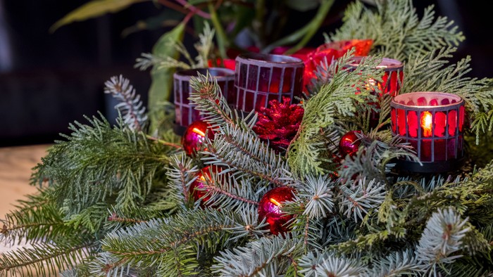 Eleganter Weihnachtskranz verziert mit Tannengrün, roten Christbaumkugeln und flackernden Kerzenlaternen.