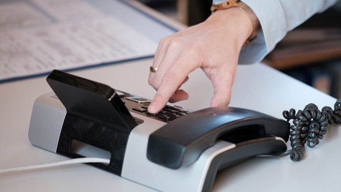 Hand greift nach Telefonhörer auf Schreibtisch
