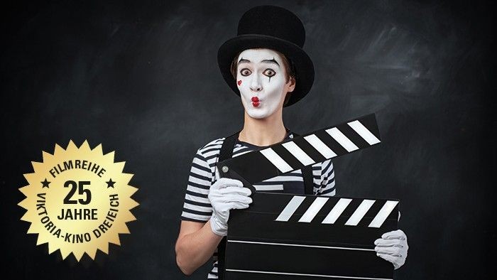 Ein Clown in Weißschminke hält eine Filmklappe und feiert 25 Jahre einer Filmreihe im Kino.