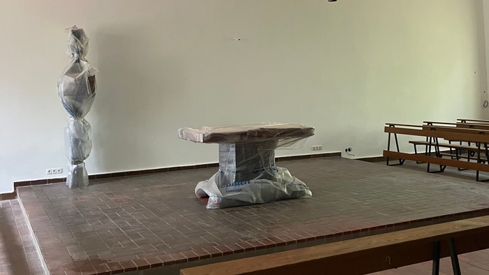 Moderner Galerieraum mit abstrakten Skulpturen und einer rot beleuchteten Wandpräsentation, minimalistischen Tischen und Bänken.