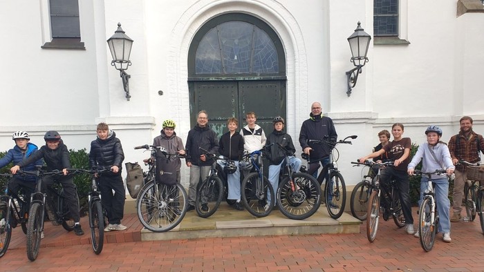 Eine Gruppe von Radfahrern, die draußen vor einem Gebäude mit ihren Fahrrädern auf einem gepflasterten Platz posieren.