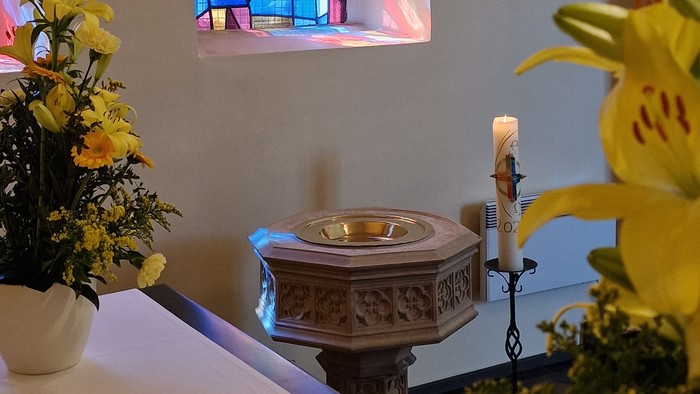 Buntes Kirchenfenster über Altartisch mit Kerze und Blumen