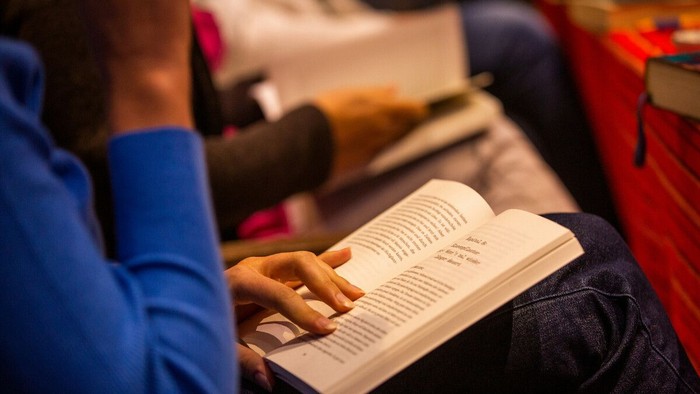 Eine Person, die in einer gemütlichen, schwach beleuchteten Umgebung ein Buch liest, umgeben von anderen.