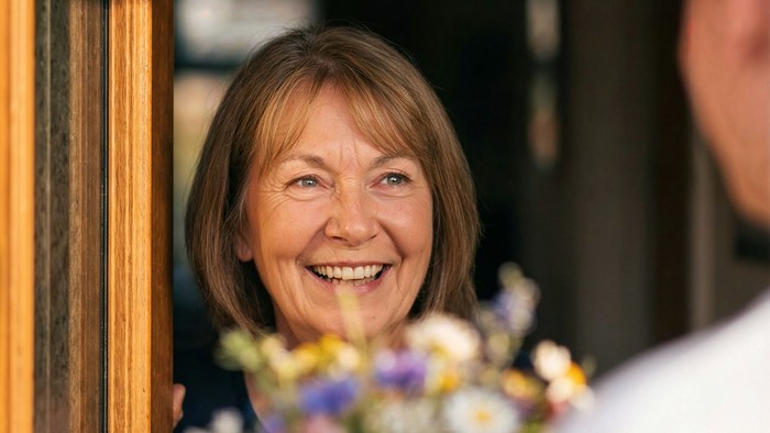 Frau in offener Tür und Besucher mit Blumenstrauß