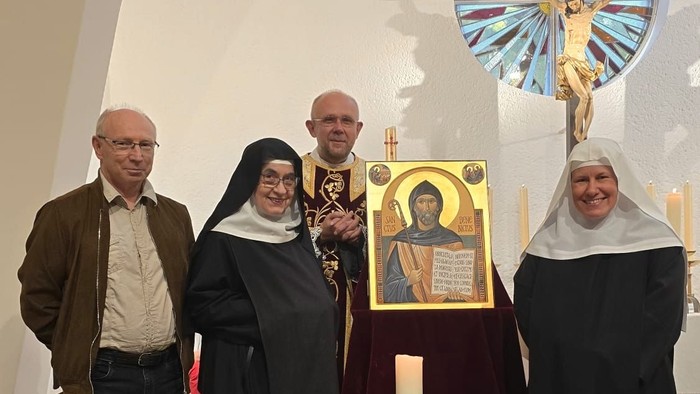 Gruppe von Menschen, darunter Nonnen, die in einer Kirche in der Nähe eines religiösen Symbols und Altars mit einem Kreuz stehen.