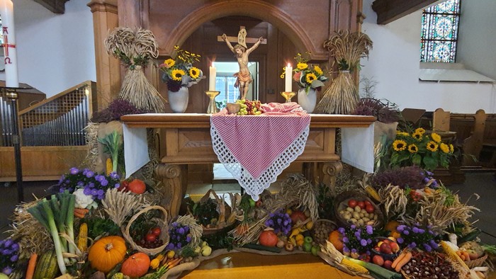 Lebendige Altargestaltung mit saisonalem Obst, Blumen und Weizengarben unter einem Kruzifix in einer Kirche.