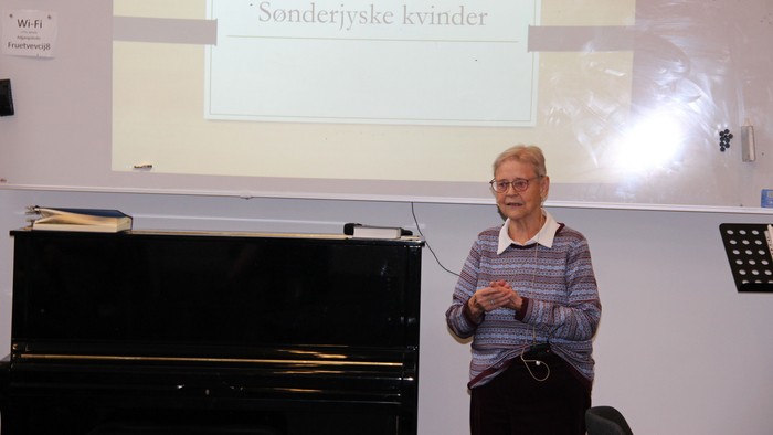 Lis Mikkelsen står forrest i billedet og fortæller, mens man i baggrunden kan se en skærm med ordene