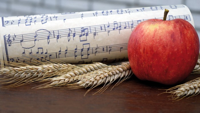 Ein roter Apfel liegt neben Notenpapier und Weizenähren auf einem Holztisch