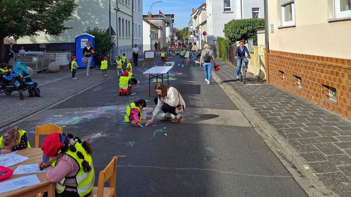 Eine Gruppe Kinder in Neonwesten spielt und malt auf einer gesperrten Otsstraße.