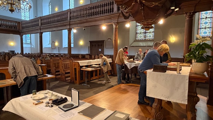 Im Kirchenraum beugen sich Menschen über ausgestellte Bücher, Geschirr und Informationen.
