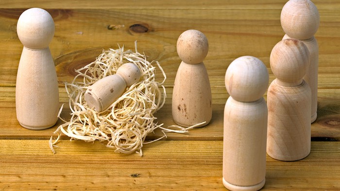 Handgeschnitzte Holzfiguren, arrangiert mit Stroh und einem zylindrischen Holzstück auf einer Holzfläche.