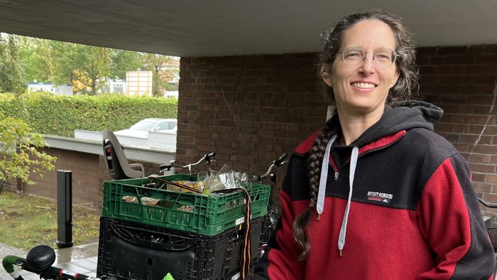 Eine junge Frau steht neben einem Lastenrad mit Obst und Gemüse.