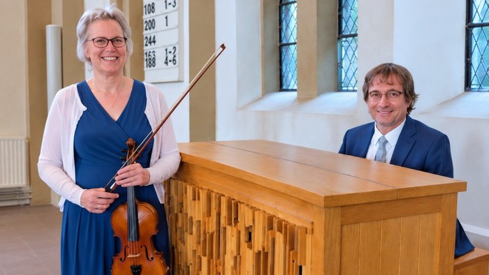 Zwei Personen posieren mit einem Cello und einer Orgelkonsole in einer Kirche.