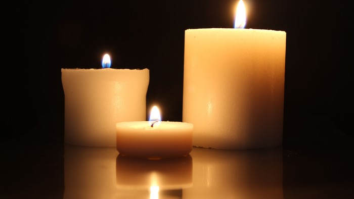 Three lit candles of varying sizes on a reflective surface.