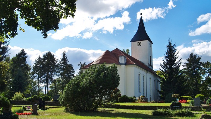 Weiße Kirche mit hohem Turm auf grünem Rasen bei klarem Himmel