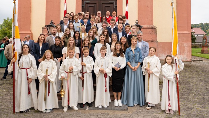Gruppe von Kindern und Erwachsenen in zeremoniellen weißen Roben posiert vor einer Kirche für eine offizielle Veranstaltung.