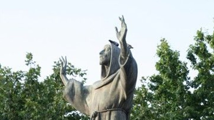 Stutue des Franz von Assisi mit erhobenen Armen gen Himmel auf steinernem Sockel