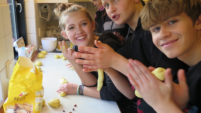 Tre børn sidder ved en køkkenbord og laver kager.