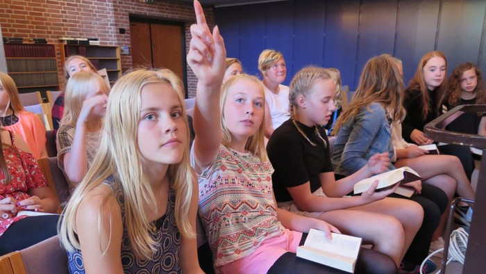 En gruppe skolepiger i klassesalen med en pige der hejer hånden.