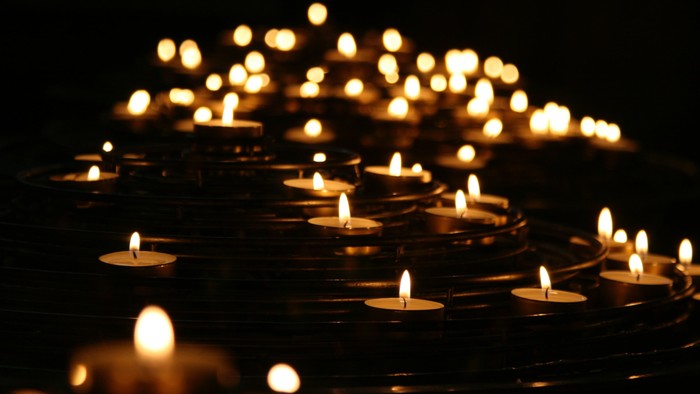 Warm leuchtende Kerzen, die in einem kreisförmigen, beleuchteten Muster vor dunklem Hintergrund angeordnet sind.