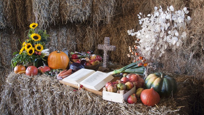 Ein Erntedankarrangement mit Heuballen, Obst, Gemüse, Blumen und einem Kreuz