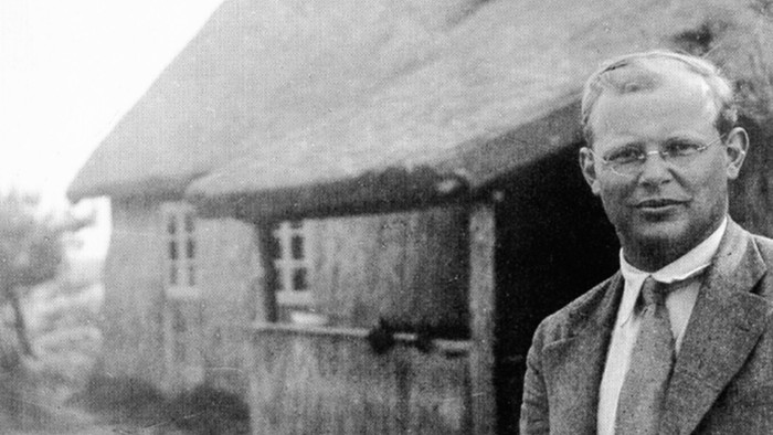 Mann in Anzug vor altem Haus mit Strohdach