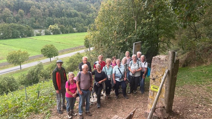 Eine Gruppe Wanderer posiert gemeinsam auf einem malerischen Pfad mit Blick auf ein üppiges grünes Tal und eine Straße.