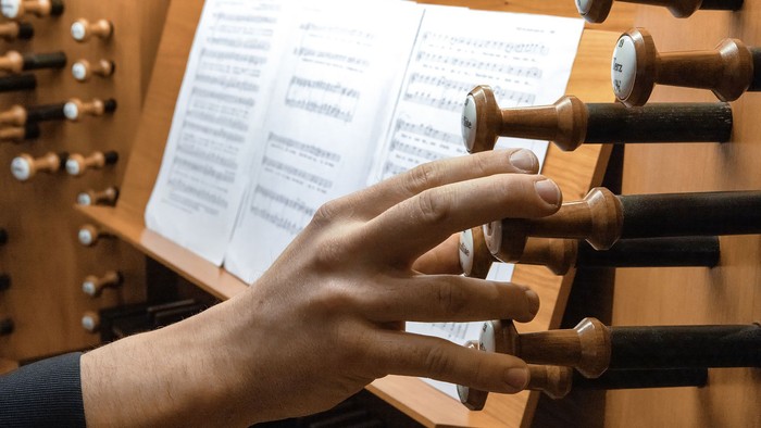 Eine Person, die eine Orgel spielt und dabei mit den Händen die Register am Spieltisch einstellt.