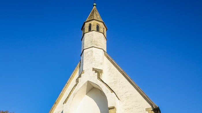 Weiße Kirche mit hohem Turm und spitzem Dach unter blauem Himmel