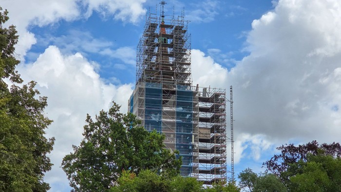 Ein Hochhaus im Bau mit Gerüsten und Kränen vor einem teilweise bewölkten Himmel.