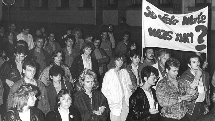 Eine Gruppe von Demonstranten hält ein Schild mit der Aufschrift *„So viele Worte, was nun?“* während einer Kundgebung.