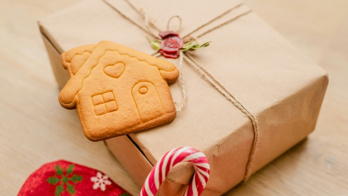 Eine Geschenkbox in braunes Papier eingepackt, verziert mit einem Lebkuchenhaus-Keks und einer Zuckerstange.