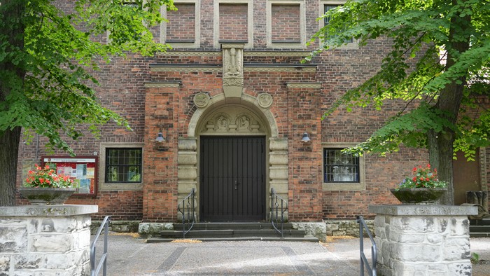 Historischer Ziegelsteingebäude-Eingang, eingerahmt von Grünpflanzen und Steintreppen.