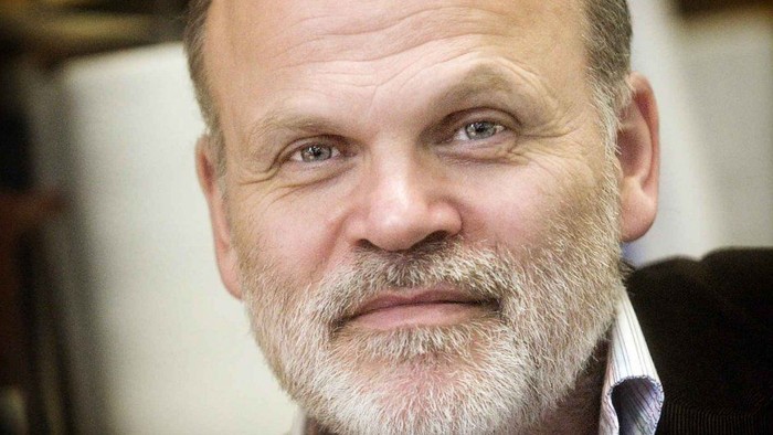 En midaldrende mand med skæg og overskæg iført en mørk jakke, der smiler let.