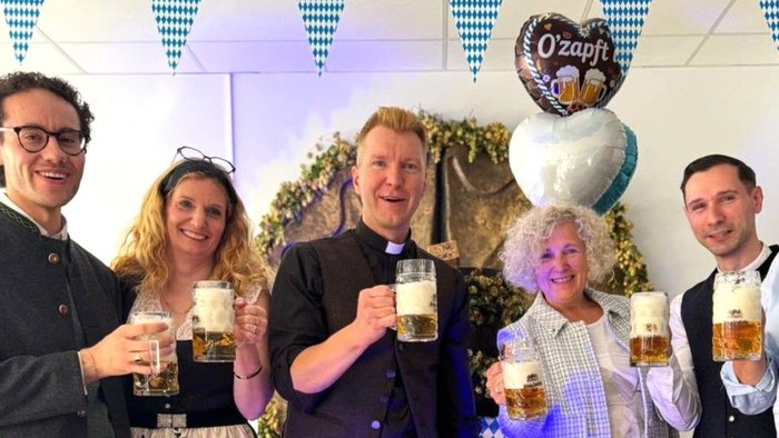 Die Gruppe feiert mit Getränken, trägt festliche Kleidung und traditionelle bayerische Trachten und posiert fröhlich in Innenräumen.