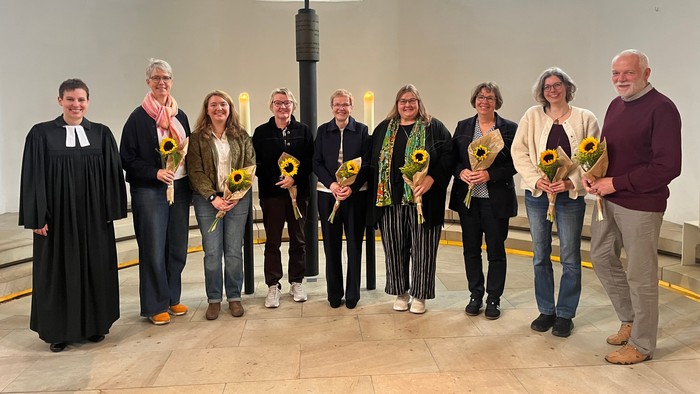 Auf dem Foto sieht man Pfarrerin Lena Stubben mit sieben Lektorinnen und einem Lektor die alle zur Begrüßung eine Sonnenblume bekommen haben.