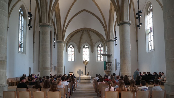 Hier sieht man ein Blick von hinten in den Kirchraum mit vollbesetzten Stühlen.