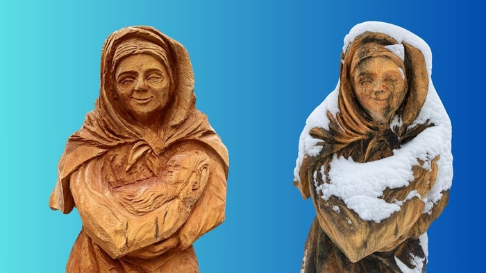To træstatuer af ældre kvinder, den ene dækket af sne, sat op mod en blå baggrund.