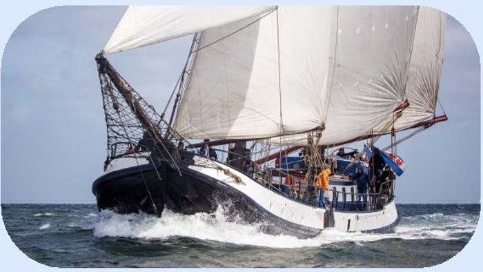 Traditionelles Segelschiff mit großen Segeln, das durch unruhige Meeresgewässer schneidet, mit Besatzung an Bord.