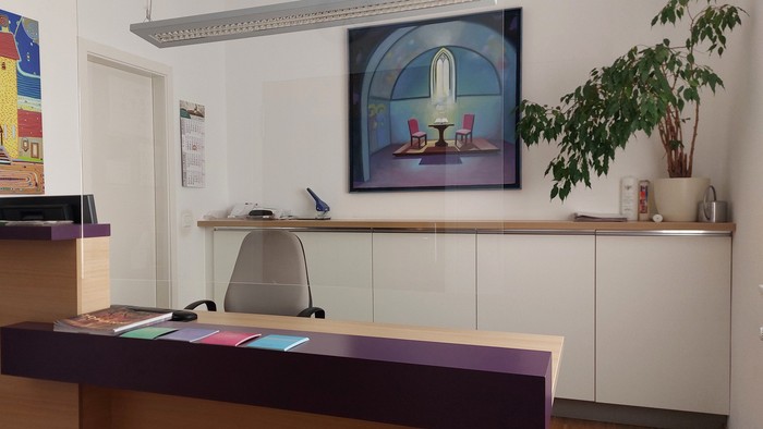 Moderner Empfangsbereich mit farbenfrohen Kunstwerken, einem Schreibtisch und einer Topfpflanze neben einem gerahmten dekorativen Gemälde.