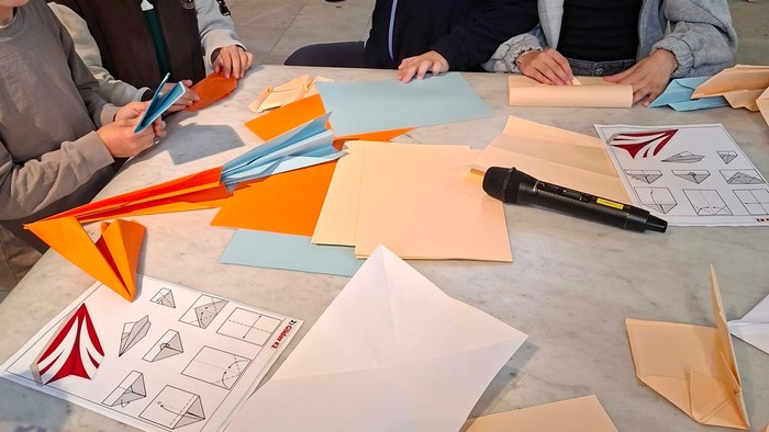 Man sieht eifrige Hände beim Versuch Papierflieger zu basteln.