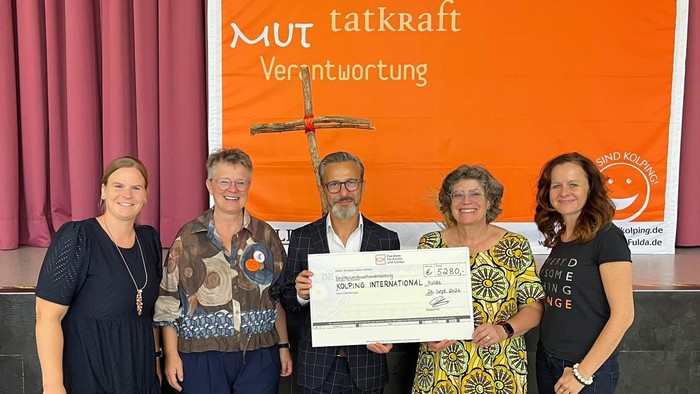 Gruppenfoto mit Urkunde und unterstütender Bühnenkulisse auf Deutsch, das Mut und Vertrauen feiert.