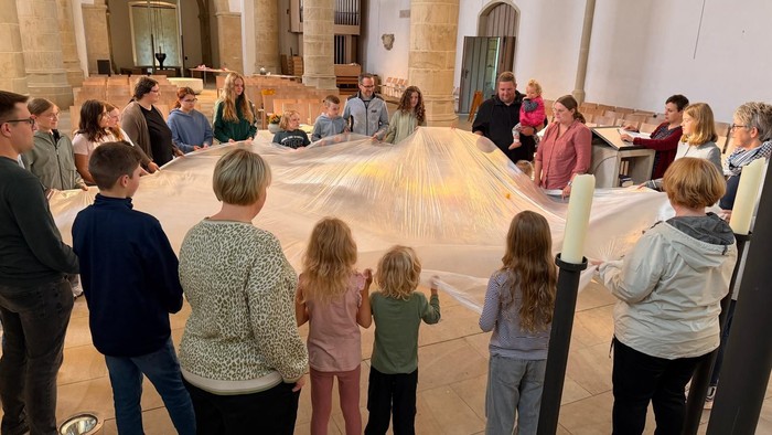 Hier sieht die Teilnehmer an der Chaoskirche im Kreis stehend, wie sie mit einer großen Folie einen