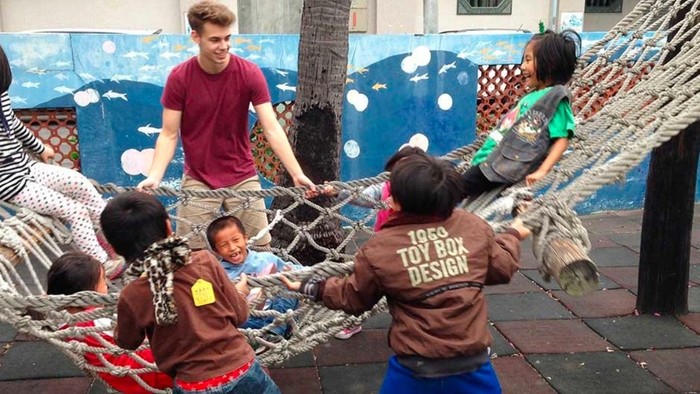 Kinder schaukeln verspielt in einer großen Outdoor-Hängematte, während Erwachsene in der Nähe beaufsichtigen.