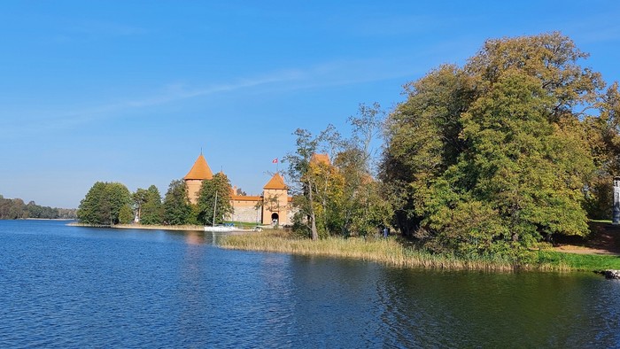 Eine friedvolle Seenlandschaft mit einem historischen Schloss, umgeben von üppigem Grün unter einem klaren blauen Himmel.