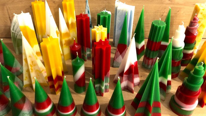 Bunte kegelförmige Kerzen in Grün, Rot, Gelb und Weiß, arrangiert auf einer Holzoberfläche.