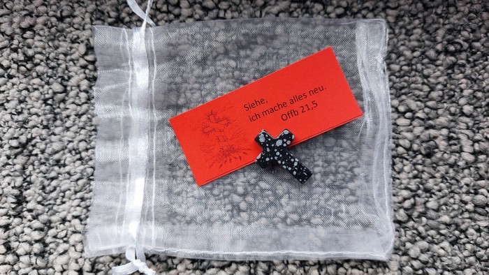 Eine kleine schwarze Stecker-Ohrring-Verpackung mit rotem Etikett und deutschem Text auf Kieselstein-Hintergrund.