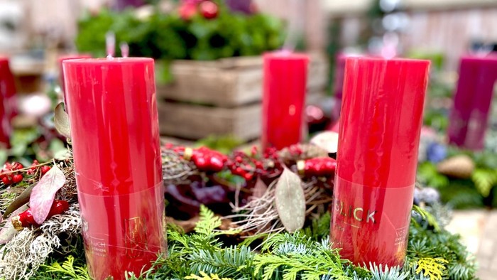 Zwei rote Kerzen auf einem Adventskranz aus Tannenzweigen und Deko.