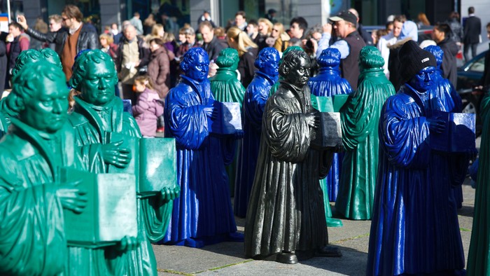 Eine Gruppe von Menschen in grünen und blauen Kostümen marschiert auf einer Straße.